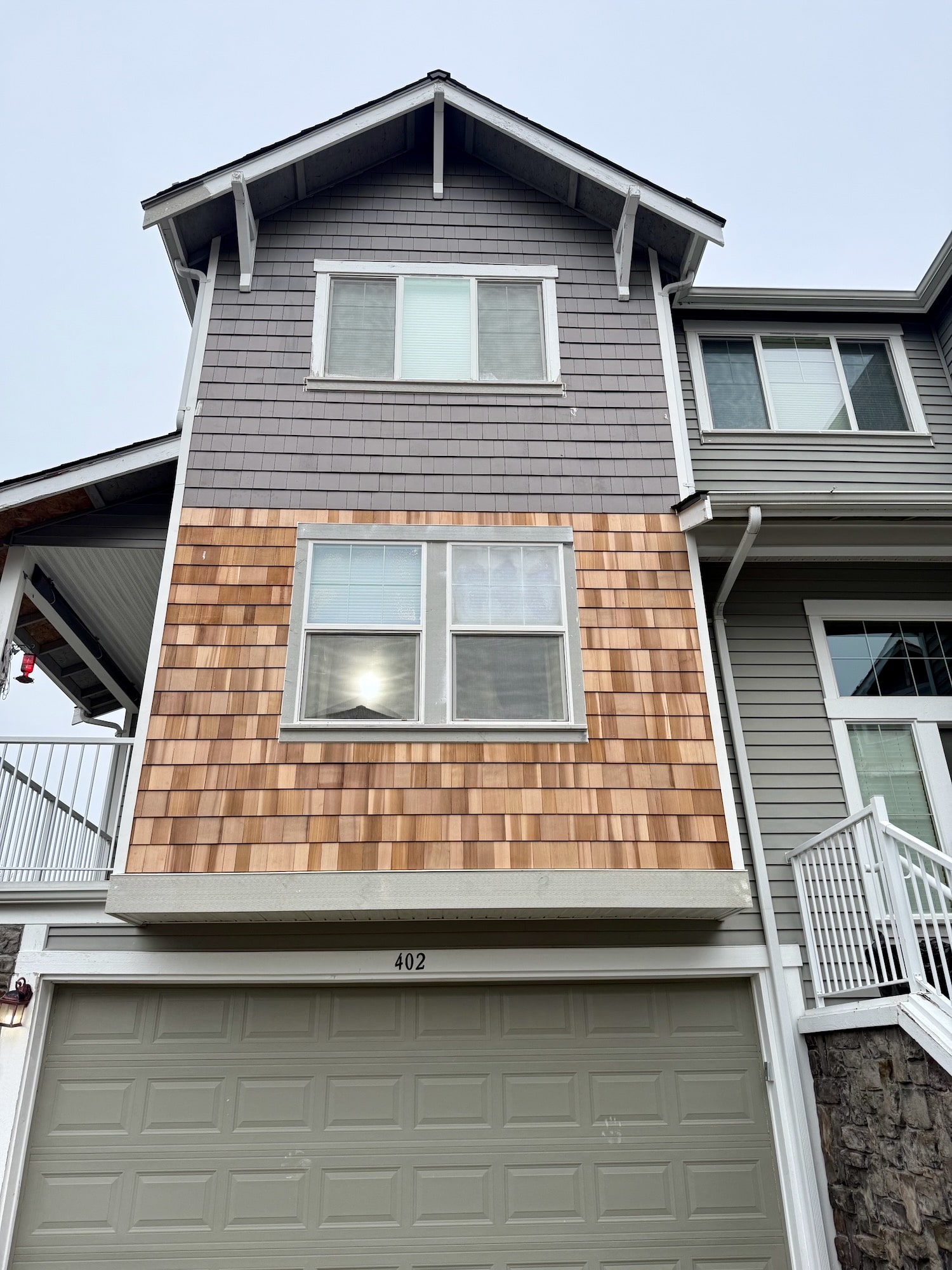 Newly installed cedar shingle siding set into a gray shingle and lap-sided wall above a garage