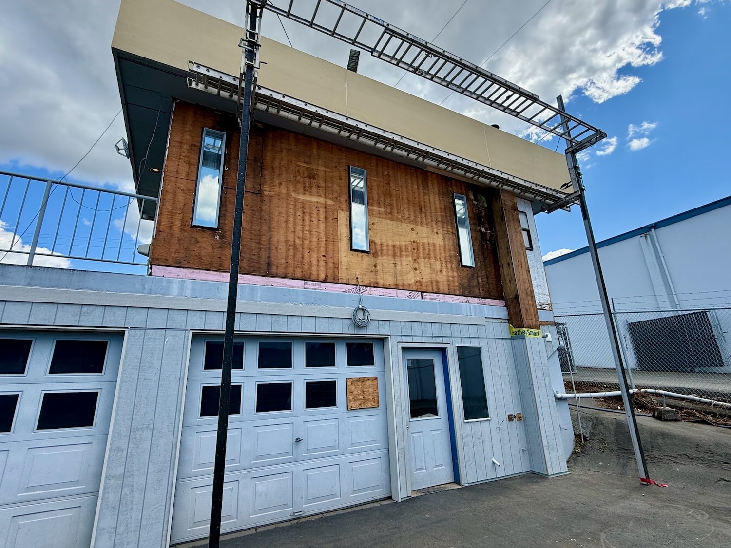 Upper-story siding stripped back to bare plywood sheathing with the weather barrier exposed at the band joist
