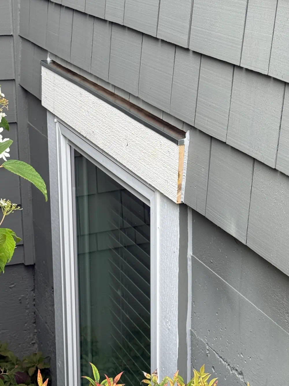 Replacement head-trim board and drip flashing fitted over a window in gray fiber cement shingle siding