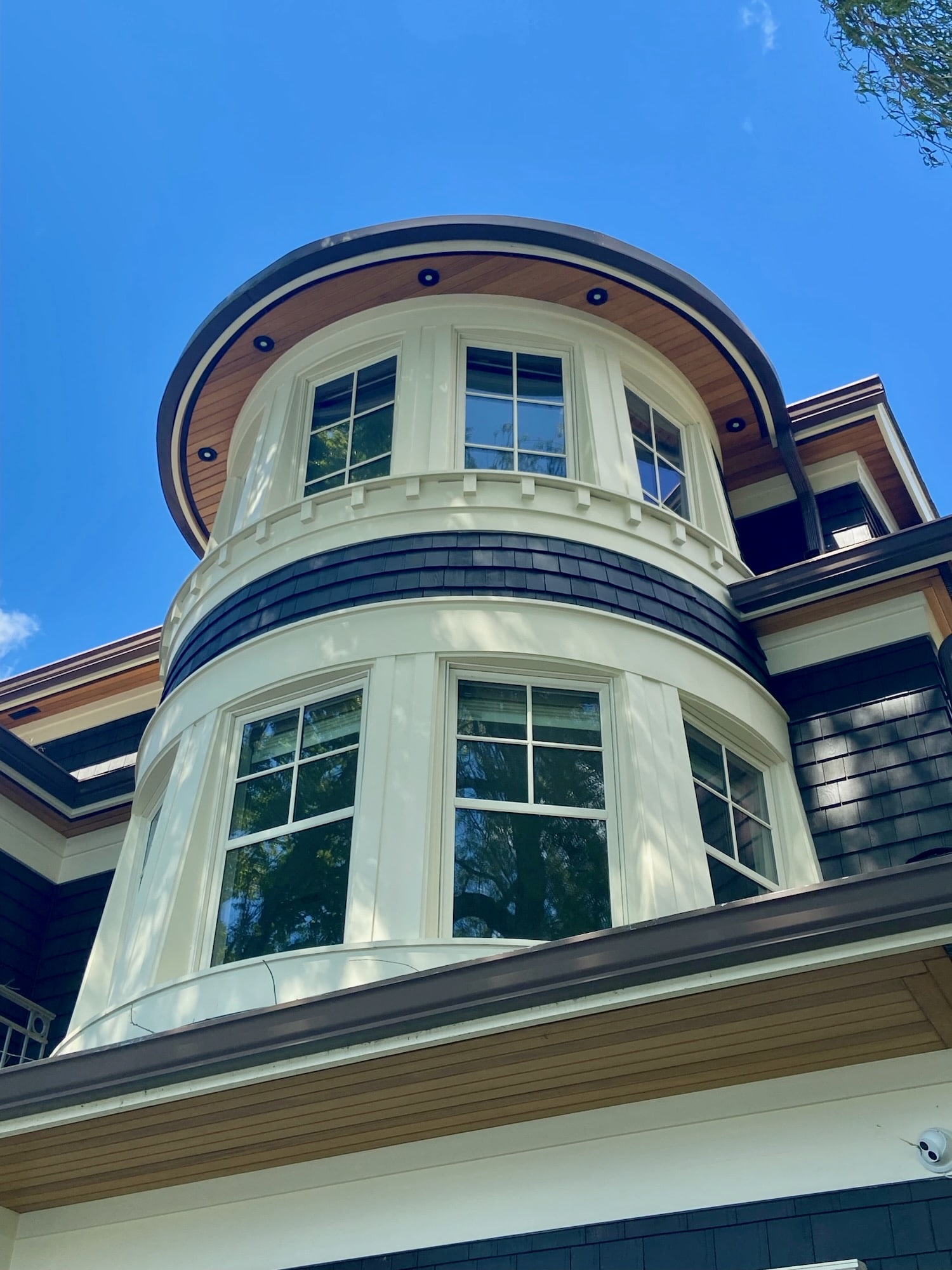 Rounded bay window tower with new white composite trim, a stained wood soffit and dark shingle siding above